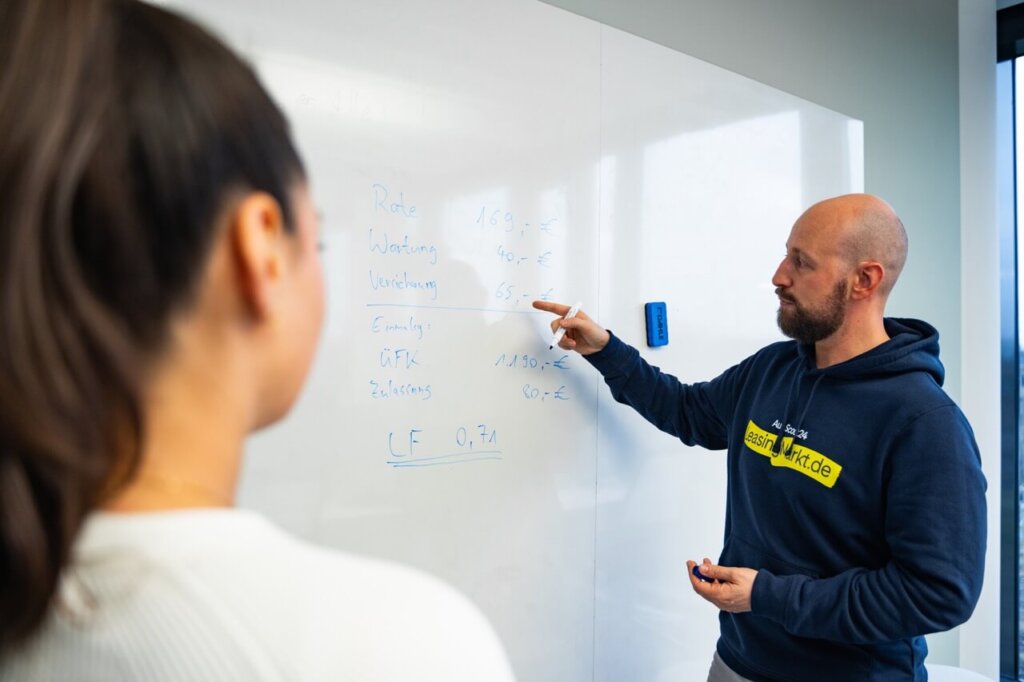 Mann und Frau stehen vor Whiteboard und berechnen Kosten